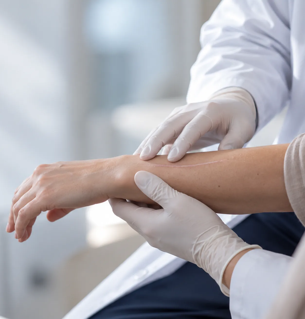 Profesional médico evaluando una cicatriz en el antebrazo de un paciente durante una consulta.